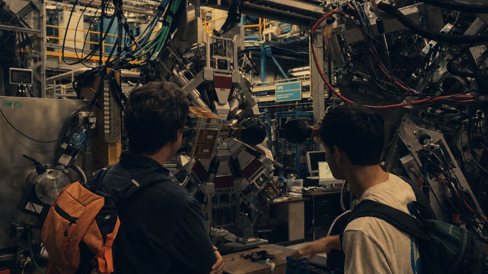 Two engineers standing in front of a large experimental machine dense with cabling and instrumentation.