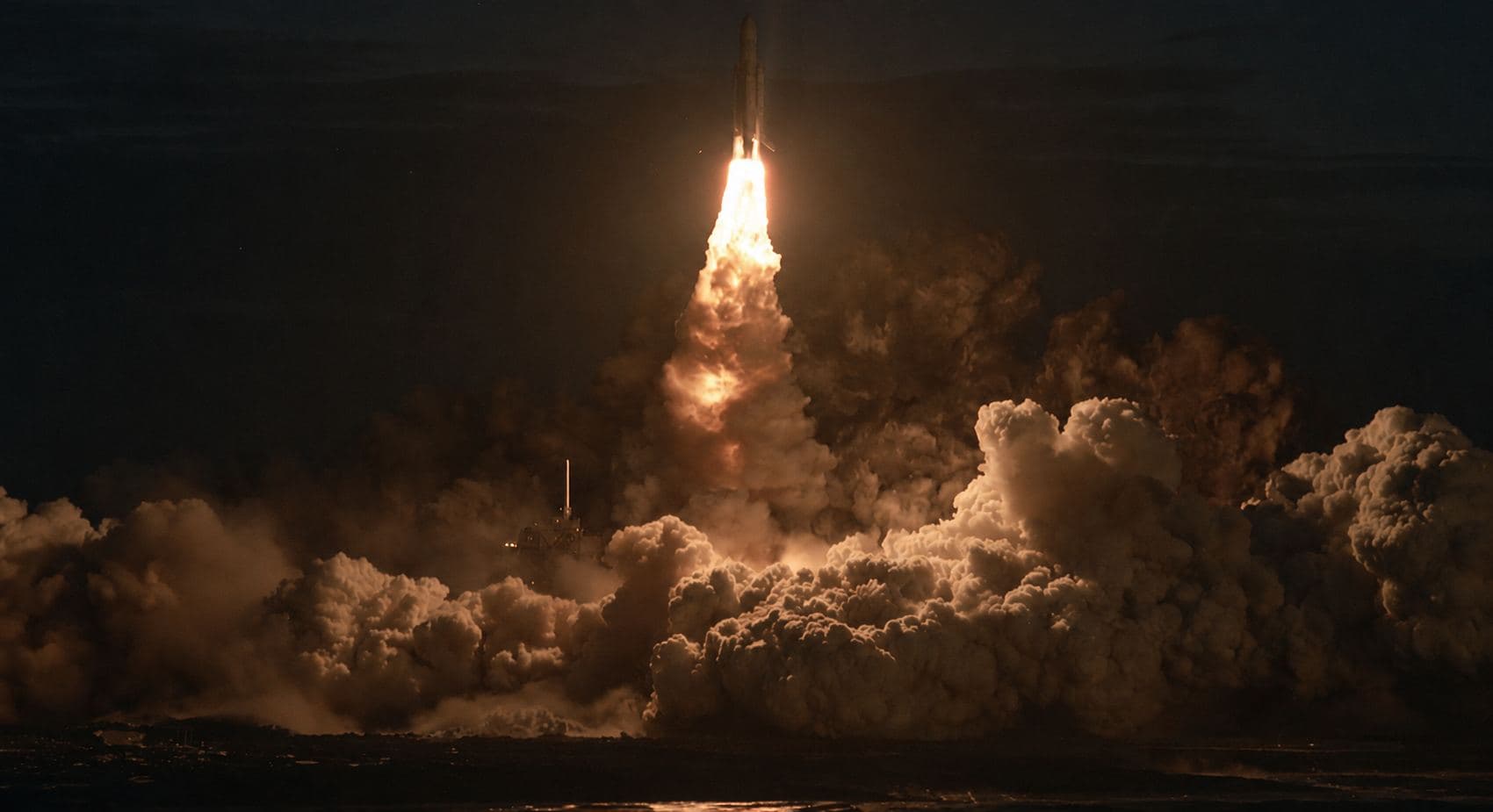 A rocket lifting off at night, engine fire lighting the steam clouds around the pad.