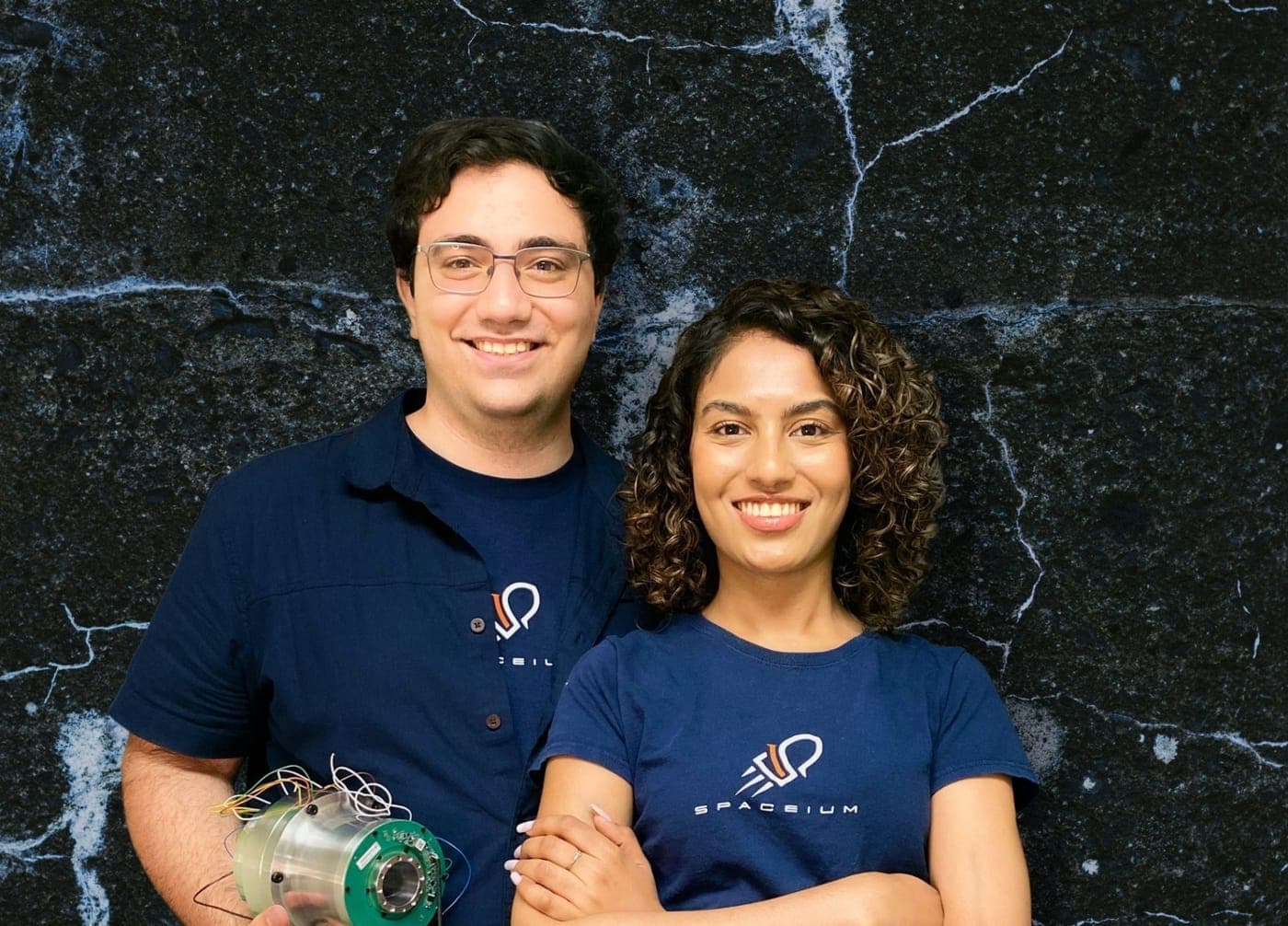 Two Spaceium co-founders in company shirts standing together, one holding a small propulsion component.