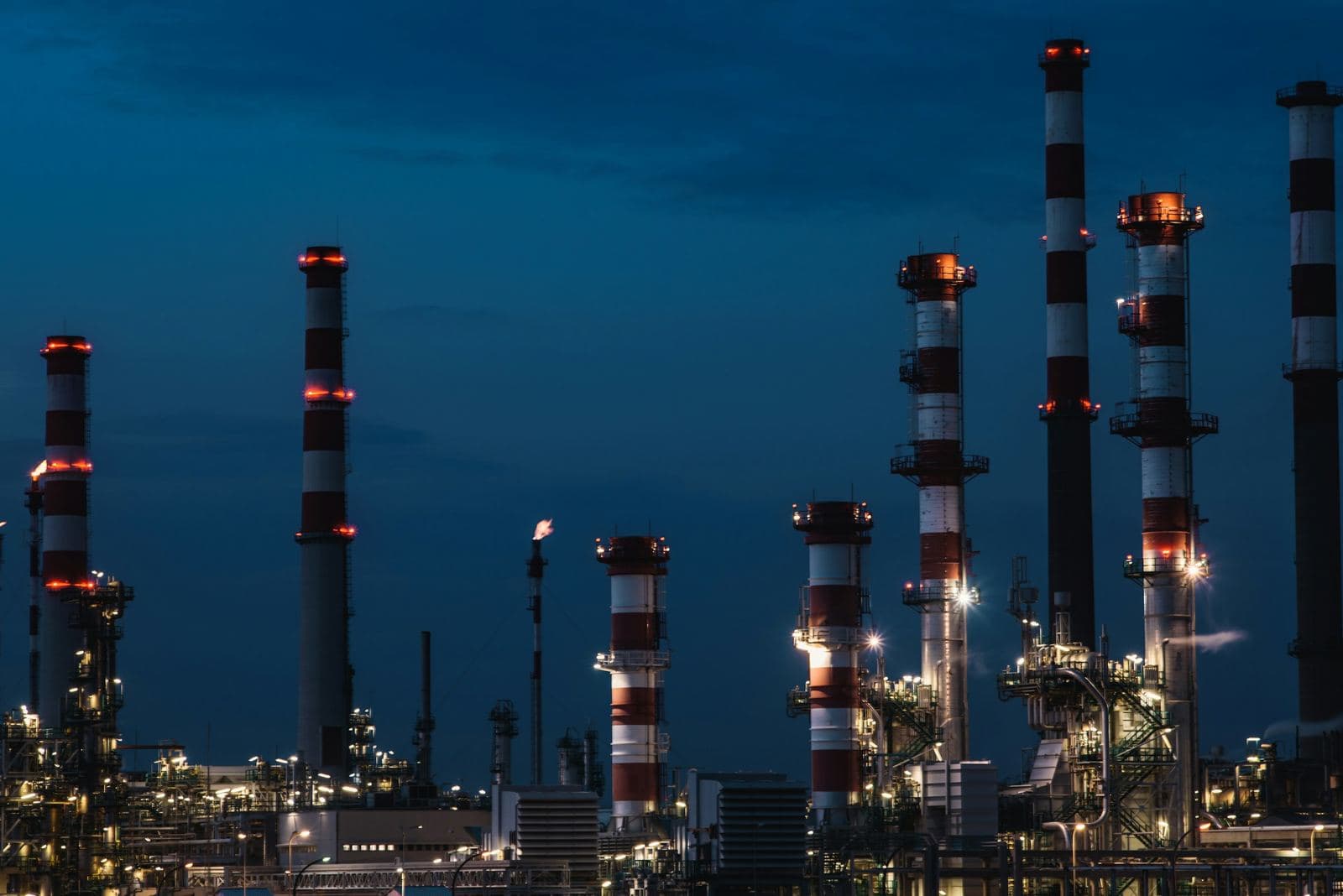 A process plant at night, its stacks and columns lit against a deep blue sky.